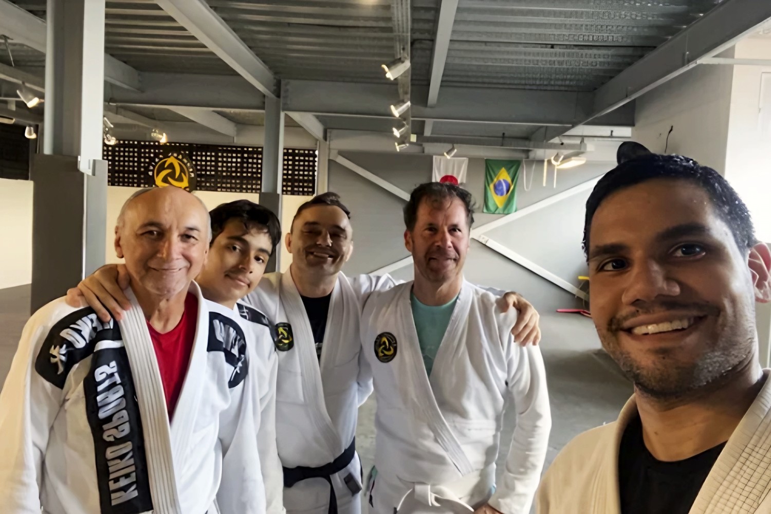 Cinco praticantes de várias idades, de kimono, sorrindo juntos no dojô